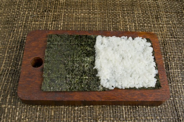 На половину листа нори выкладываем рис и распределяем его