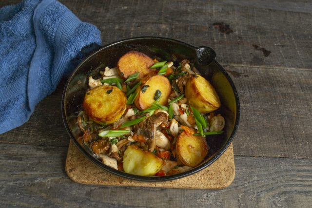 Выкладываем картошку с грибами и курицей в порционную сковородку и посыпаем зелёным луком