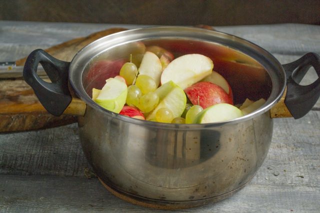 Кладём нарезанные яблоки и виноградины в кастрюлю, наливаем 50 мл воды