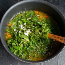 Добавляем нарезанную крапиву и чеснок, снова доводим суп до кипения и варим 5 минут