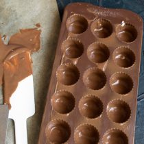 Сливаем шоколад из ячеек, убираем форму в холодильник, шоколад с бумаги соскребаем и снова растапливаем