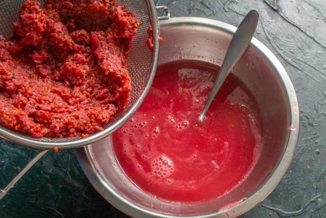 Отделяем сок от жмыха – фильтруем ягодное пюре. Ставим дуршлаг на кастрюлю, загружаем в него небольшими порциями ягодное пюре, протираем ложкой