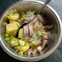 В глубокую миску кладем остывший картофель, нарезанный лук, огурцы и селедку