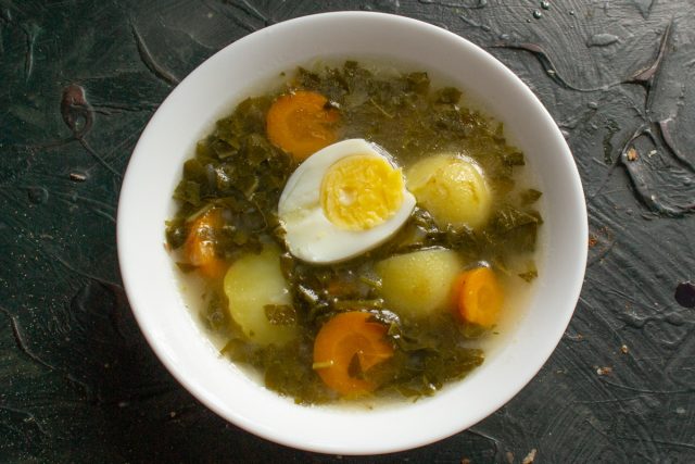 Наливаем в тарелку порцию щавелевого супа, кладём кусочек отварной курицы и половинку вареного яйца.