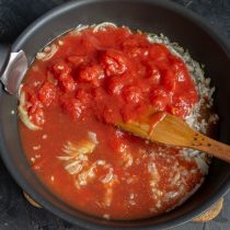 К обжаренному луку добавляем резанные консервированные томаты вместе с соком